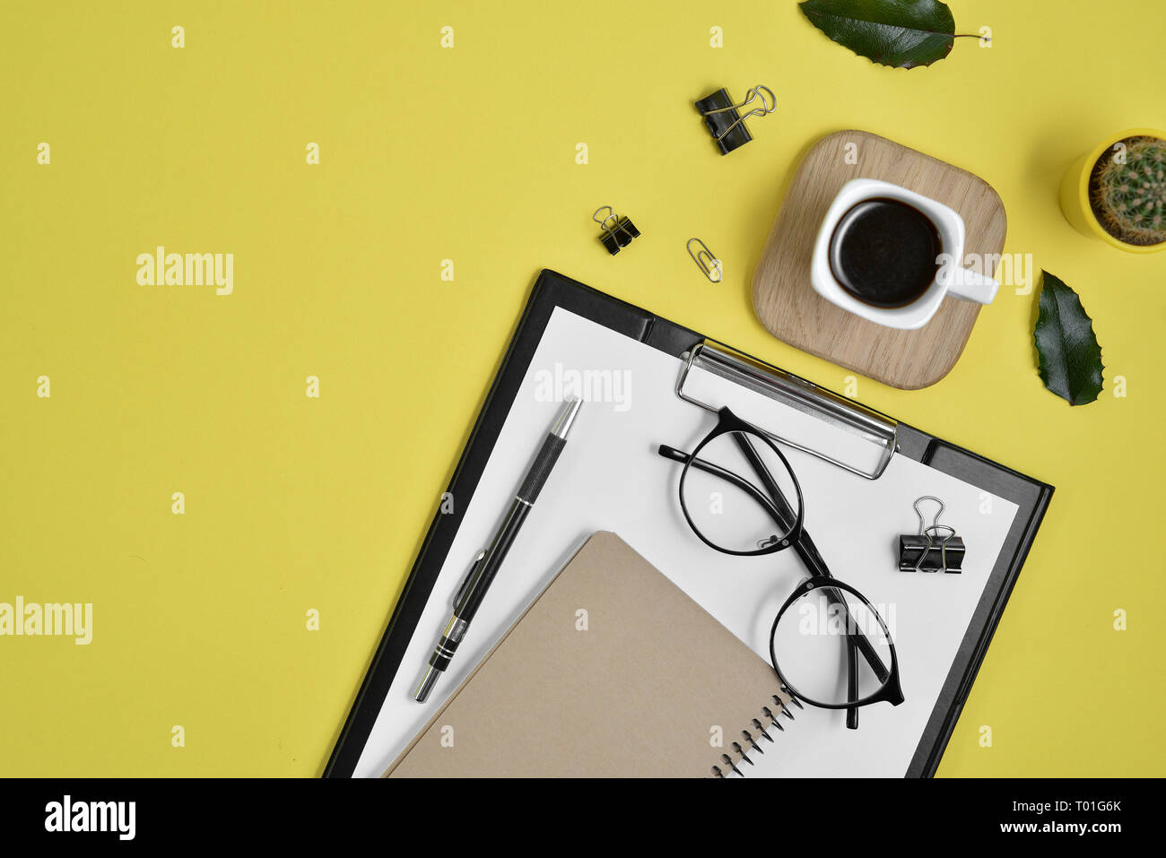 Büro Schreibtisch Arbeitsbereich mit leeren Clip Board, Bürobedarf, pen, Kaktus, grünes Blatt, Kaffeetasse und Brillen auf gelben Hintergrund. Flach, oben Stockfoto