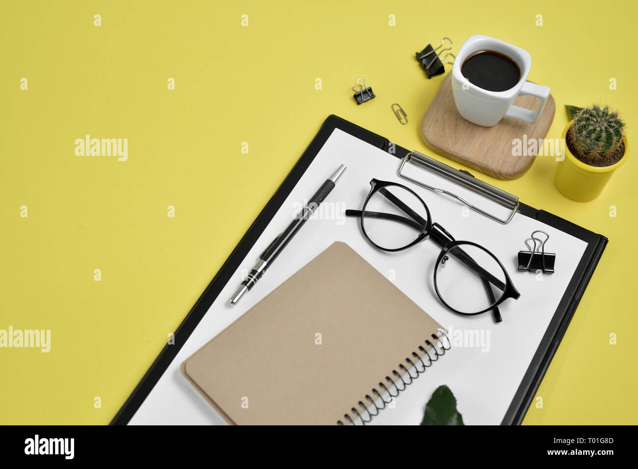 Büro Schreibtisch Arbeitsbereich mit leeren Clip Board, Bürobedarf, pen, Kaktus, grünes Blatt, Kaffee Tasse auf einem Stand aus Holz und Brillen auf Gelb backgrou Stockfoto