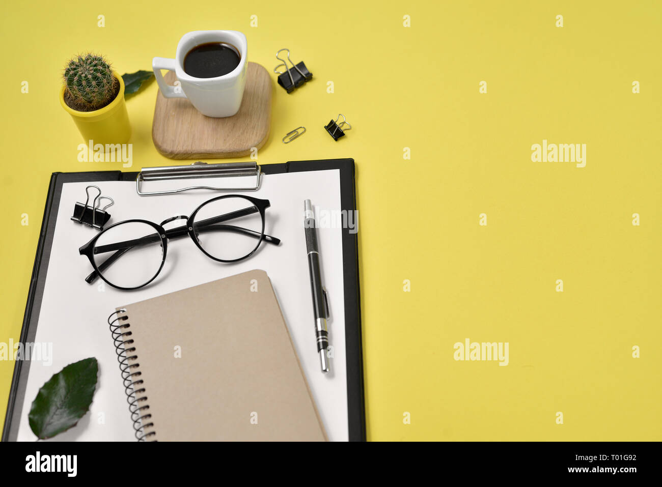 Büro Schreibtisch Arbeitsbereich mit leeren Clip Board, Bürobedarf, pen, Kaktus, grünes Blatt, Kaffee Tasse auf einem Stand aus Holz und Brillen auf Gelb backgrou Stockfoto