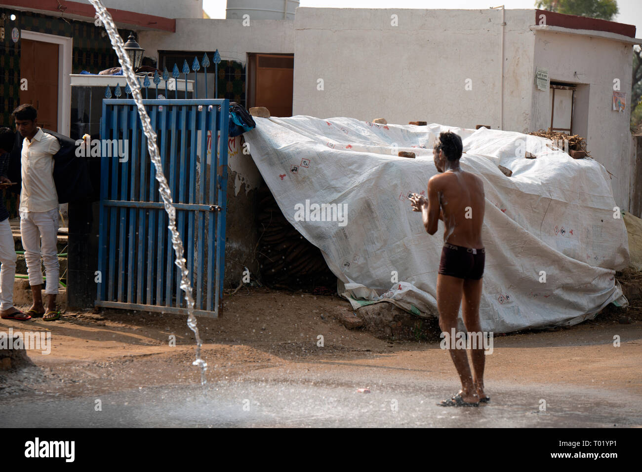 Ein Inder nimmt eine Dusche außerhalb seines Hauses. Rajasthan, Indien. Stockfoto