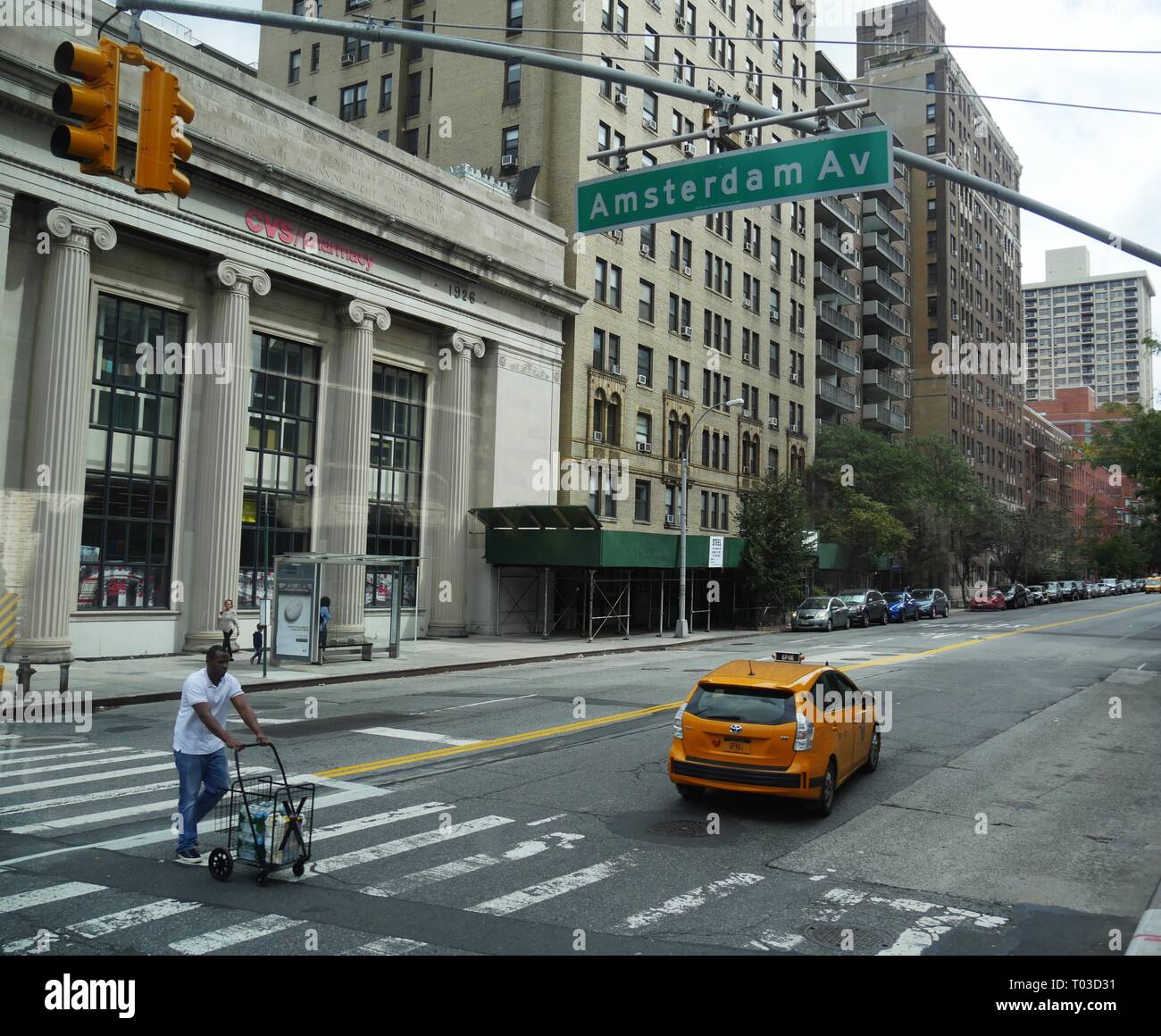 NEW YORK CITY, USA – 2017. SEPTEMBER: Ein Mann mit einem Wagen überquert die Fußgängerstraße in der Amsterdam Avenue mit einem gelben Taxi auf der Straße. Stockfoto