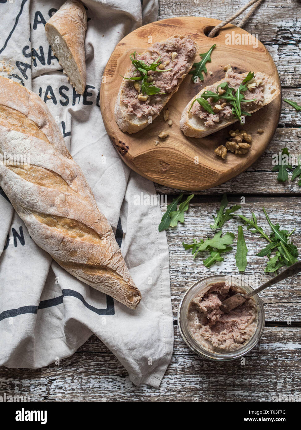 Zwei Toasts mit zarten Rillettes (Pastete) auf Weißbrot mit Rucola und Walnuss auf eine runde Holzplatte auf einem alten Holz- Hintergrund Stockfoto