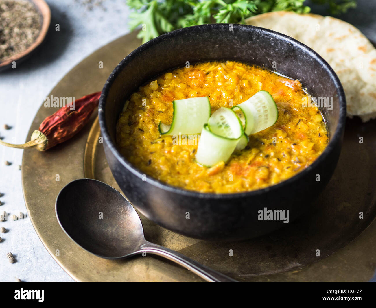 Traditionelle indische Linsensuppe Dal Suppe. Heiß und würzig Linsensuppe mit frischen Gurkenscheiben in einem schwarzen Stein Schüssel und Pita Stockfoto