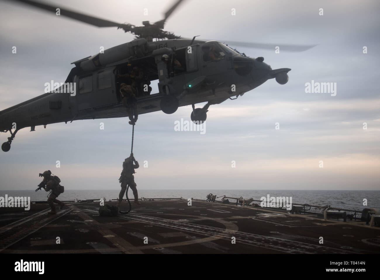 U.S. Coast Guard Maritime Sicherheit Reaktion Teammitglieder rappel auf das Flight Deck der geführten Anti-raketen-Zerstörer USS Chung-Hoon (DDG93) aus einem MH-60S Sea Hawk, Hubschrauber Meer Combat Squadron (HSC) 26, bei einem einfügevorgang Training übung im Arabischen Golf, 14. März 2019 zugeordnet. Die chung-hoon ist in die USA 5 Flotte Bereich der Maßnahmen zur Unterstützung der Marine im Einsatz für die Stabilität und Sicherheit in der Region zu gewährleisten und verbindet das Mittelmeer und den Pazifischen Raum durch den westlichen Indischen Ozean und drei strategischen Punkten ersticken. (U.S. Marine Foto von Masse Kommu Stockfoto