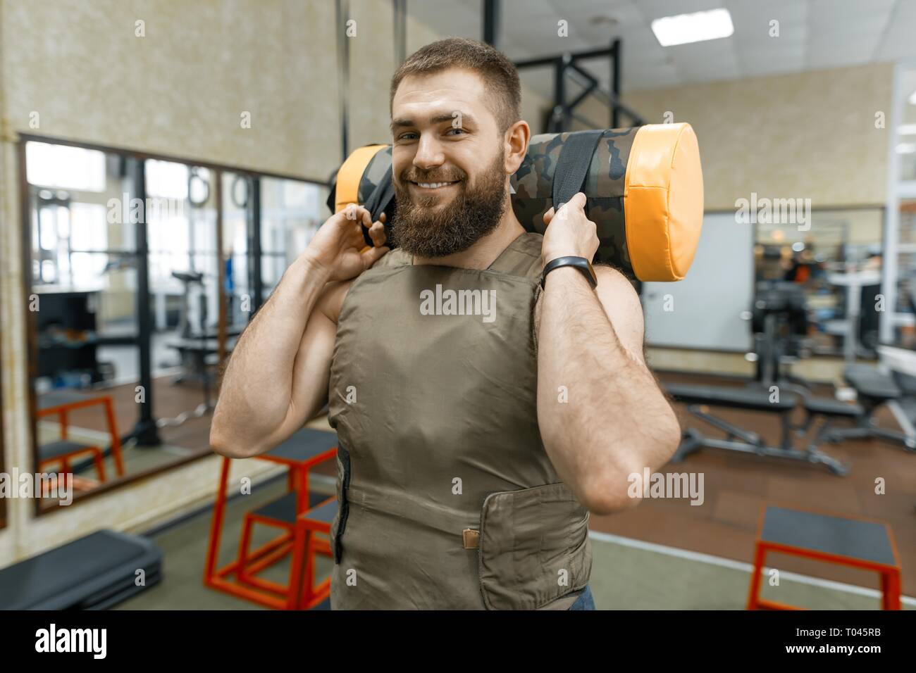 Muskulöse kaukasischen bärtiger Mann Übungen in der gewichteten Weste in der Turnhalle gekleidet, militärischen Stil. Stockfoto