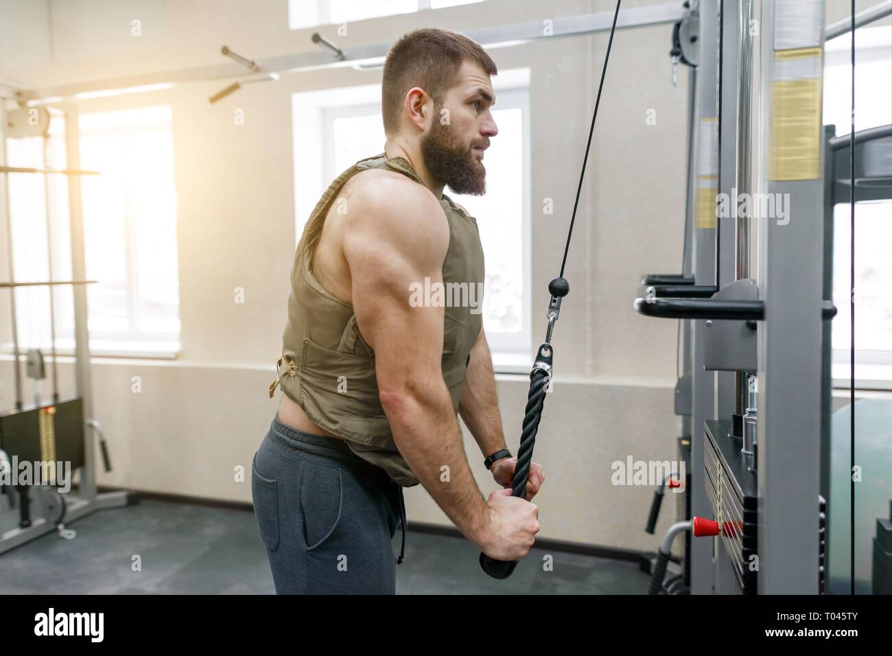 Muskulöse kaukasischen bärtiger Mann Übungen in der gewichteten Weste in der Turnhalle gekleidet, militärischen Stil. Stockfoto