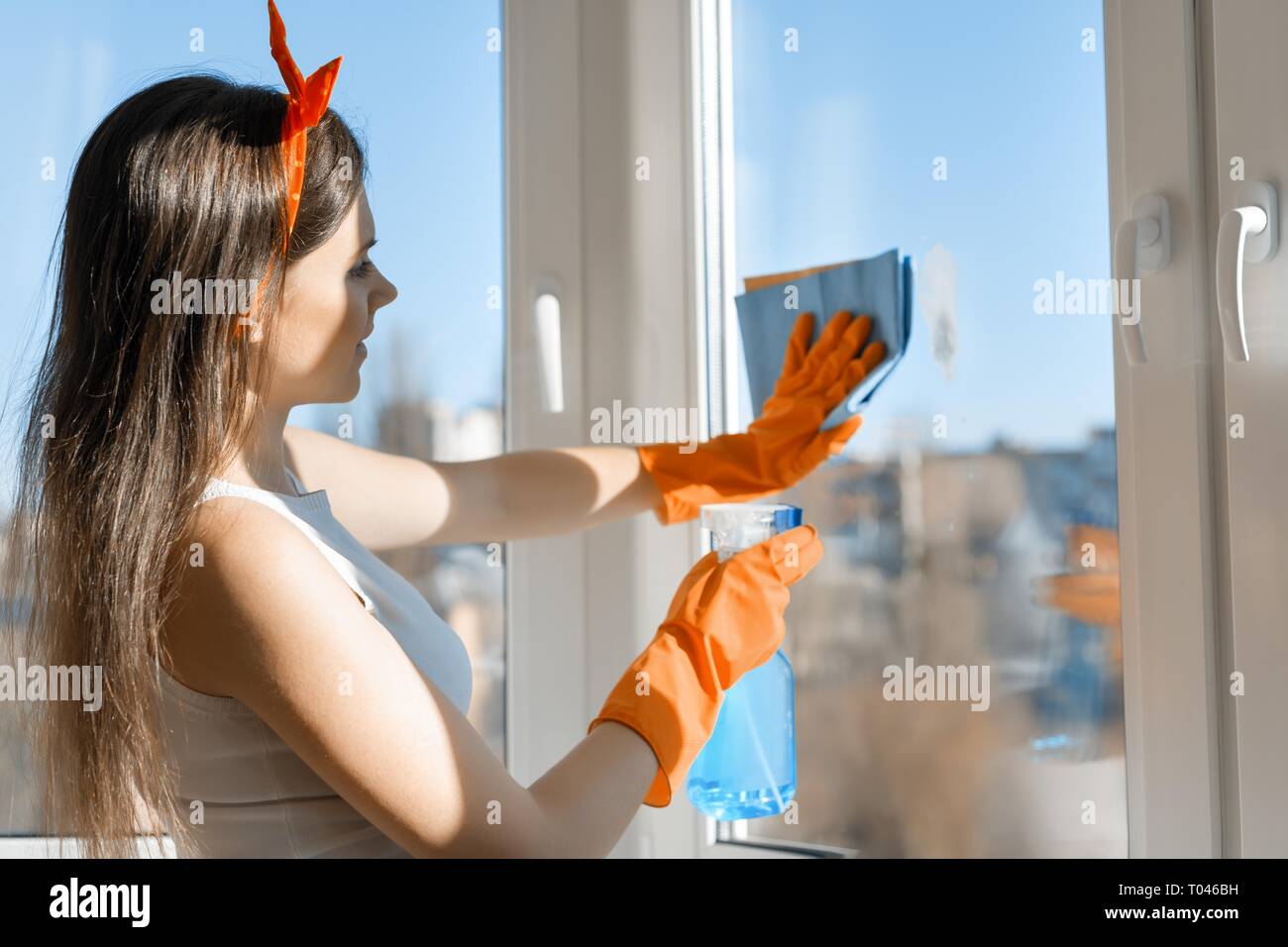 Junge lächelnde Frau Reinigung Fenster, mit Spray Glasreiniger und rag in Gummi Handschuhe, Frühjahrsputz zu Hause. Stockfoto