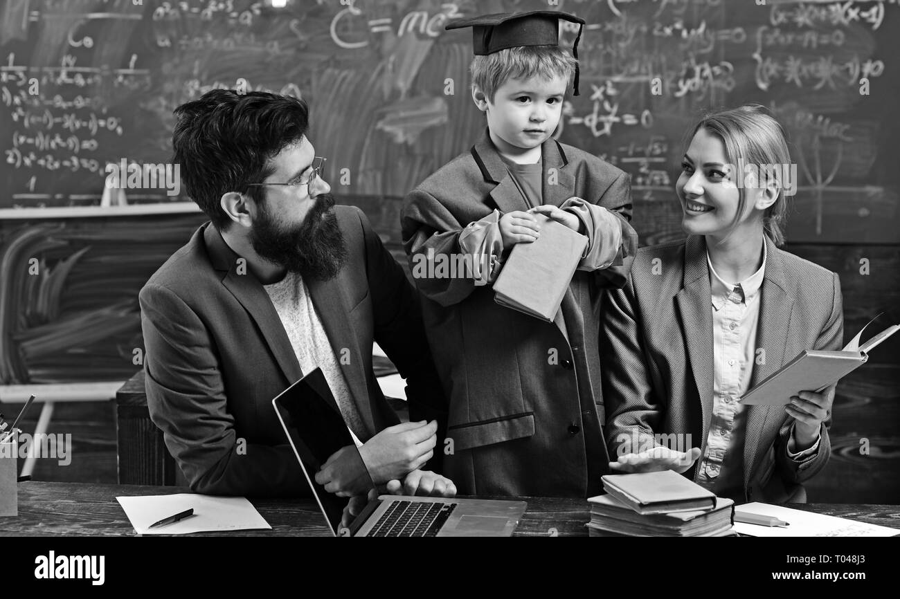 Kleines Kind spielen Schule mit Frau und Mann. Genius Sohn lesen Buch für Mutter und Vater. Familie zusammen am Schreibtisch mit Laptop. Zurück zu Stockfoto