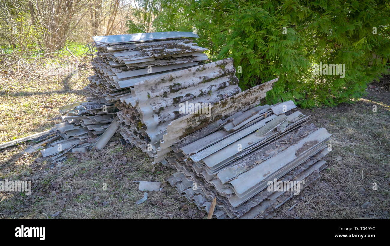 Stapel kaputte und rostige Schindeln auf dem Boden in der Mitte des Waldes mit einigen Bäumen und Pflanzen aller Stockfoto