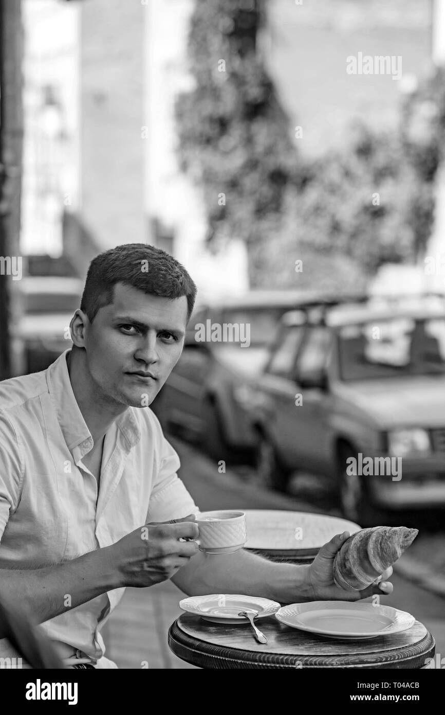 Mann essen und trinken Kaffee in Street Cafe. Macho genießen Tasse Kaffee und Croissant auf Urban outdoor. Essen und Trinken Konzept Stockfoto