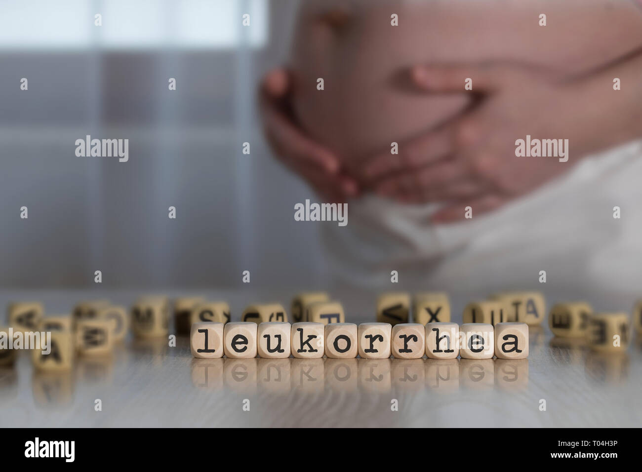 Wort LEUKORRHEA aus Holz Buchstaben. Schwangere Frau im Hintergrund Stockfoto