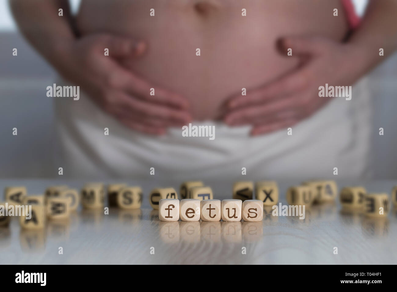Wort Fötus aus Holz Buchstaben. Schwangere Frau im Hintergrund Stockfoto