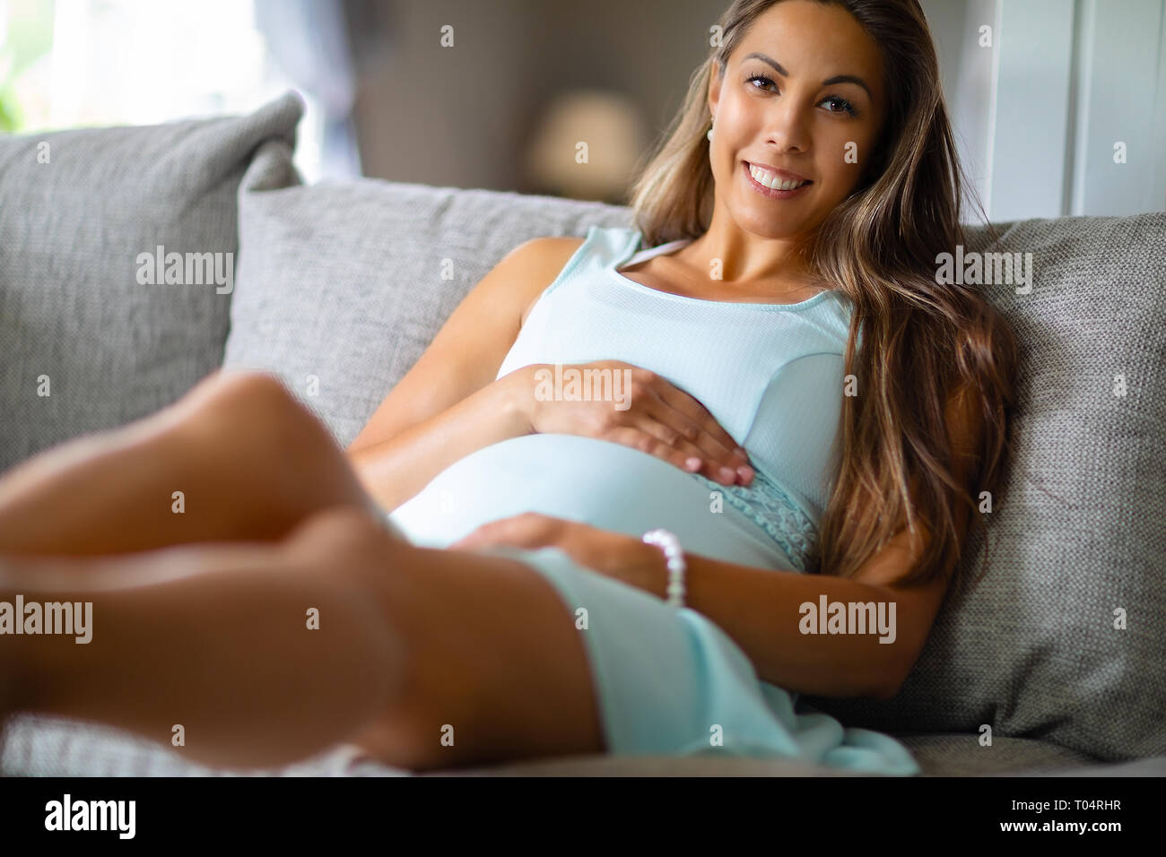Positive schwangere Frau in Kleid auf dem Sofa home Stockfoto
