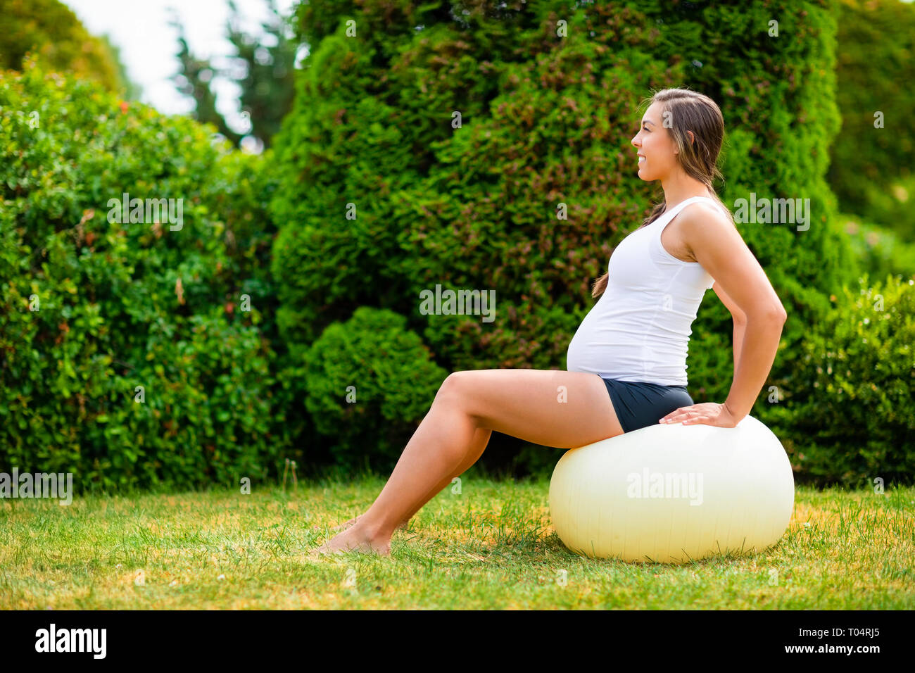 Schwangere Frau sitzt auf Yoga Ball im Park Stockfoto