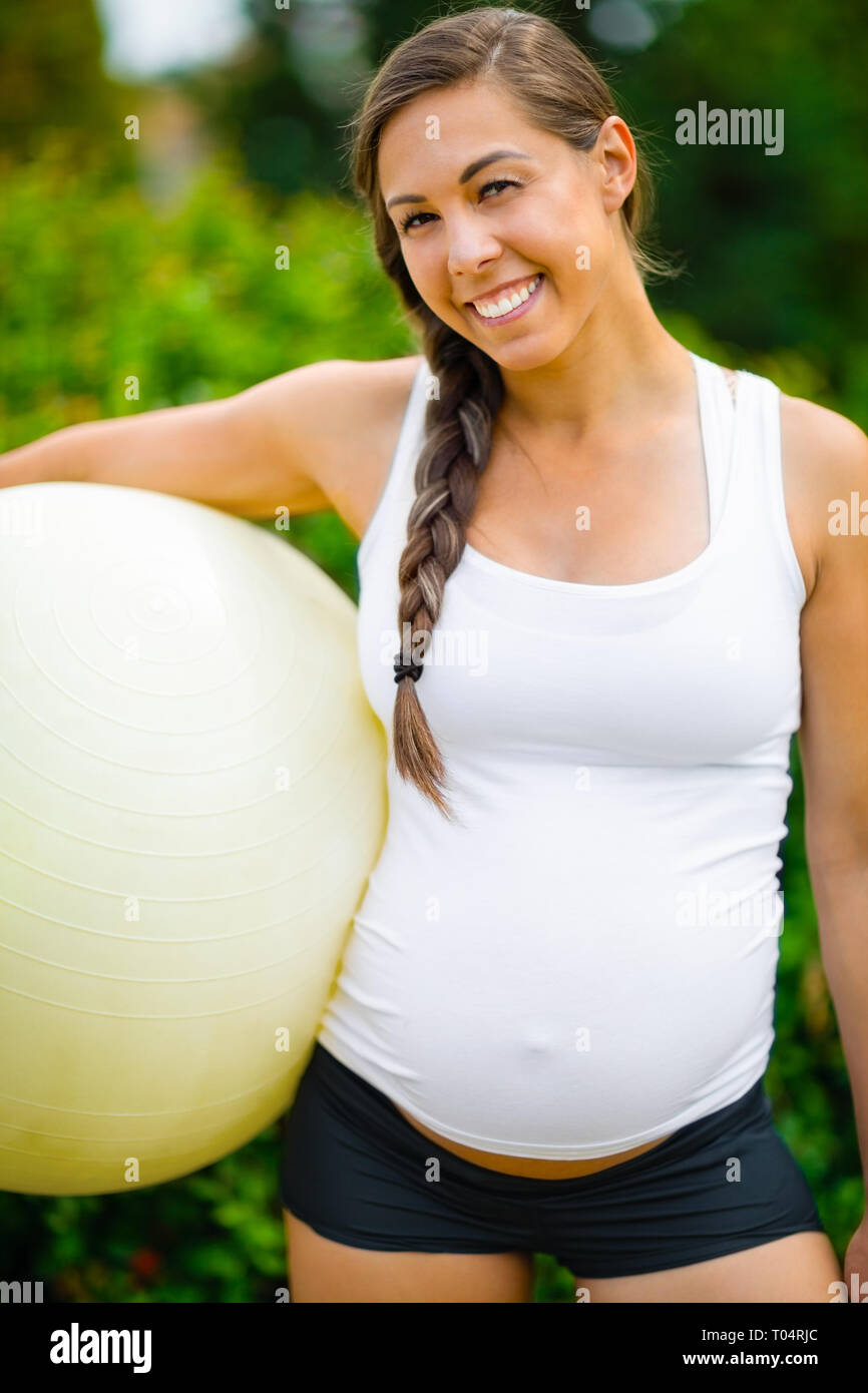 Lächelnde Junge werdende Mutter Holding Fitness Ball im Park Stockfoto