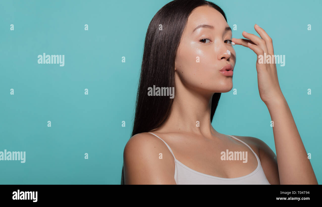 Schöne Frau Anwendung Feuchtigkeitscreme ihre Nase gegen den blauen Hintergrund.. Frau Anwendung beauty Creme im Gesicht. Stockfoto