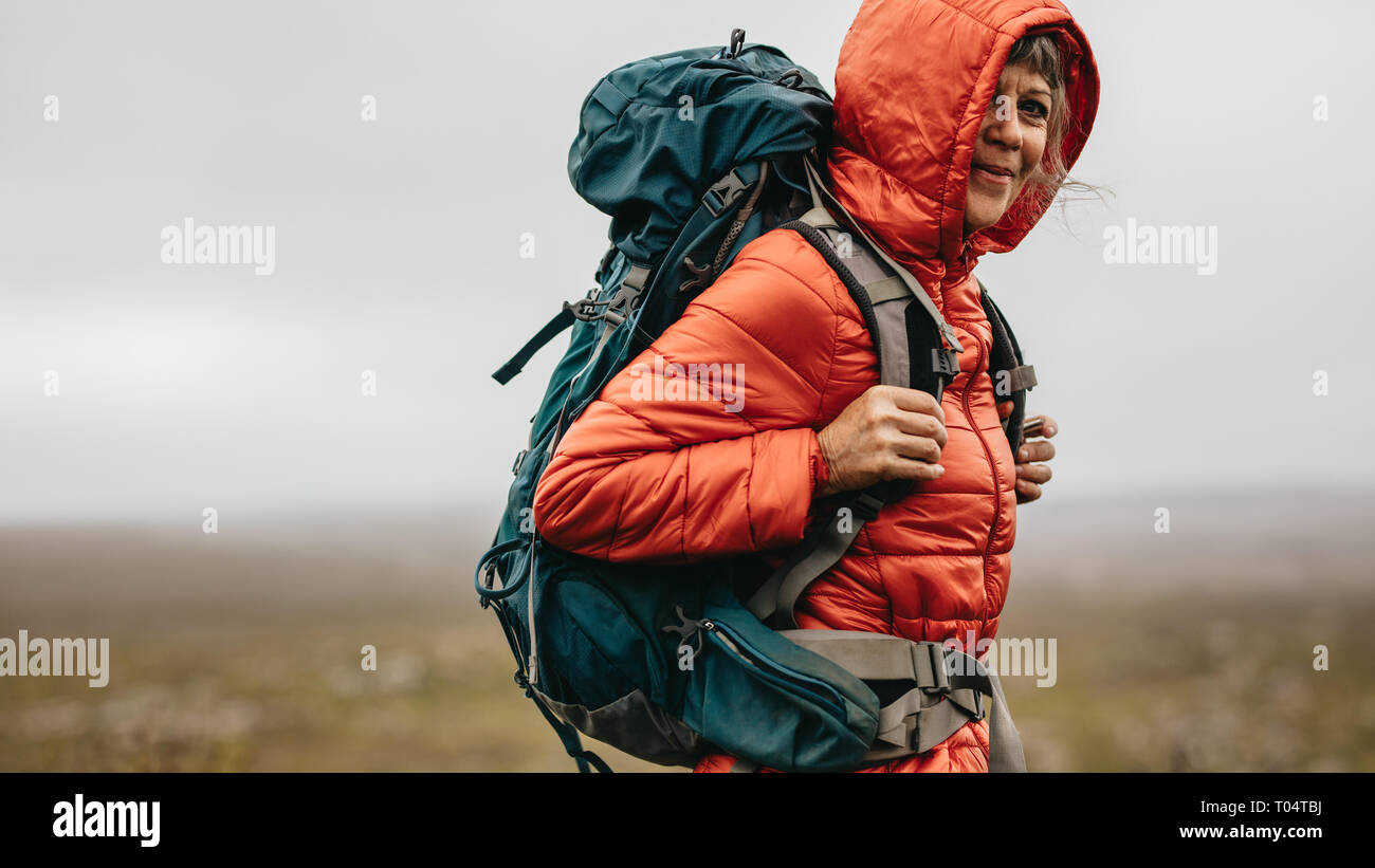 Seitenansicht einer Frau Wanderer stehen auf einem Hügel. Ältere Frau trägt ein T-Shirt und einem Rucksack stand auf der Spitze eines Hügels, während einer Wanderung. Stockfoto