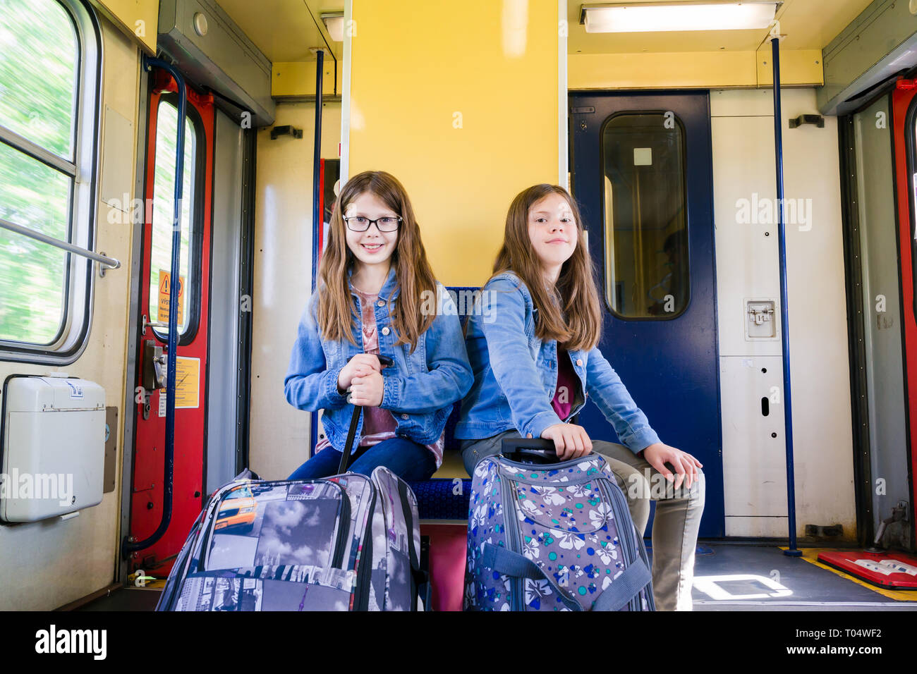 Zwei glücklich lächelnde Mädchen Kinder oder junge Jugendliche mit Rädern Kabine Koffer Taschen sitzen auf einem Zug bei einer Geschwindigkeit in Tschechien, Mitteleuropa Stockfoto