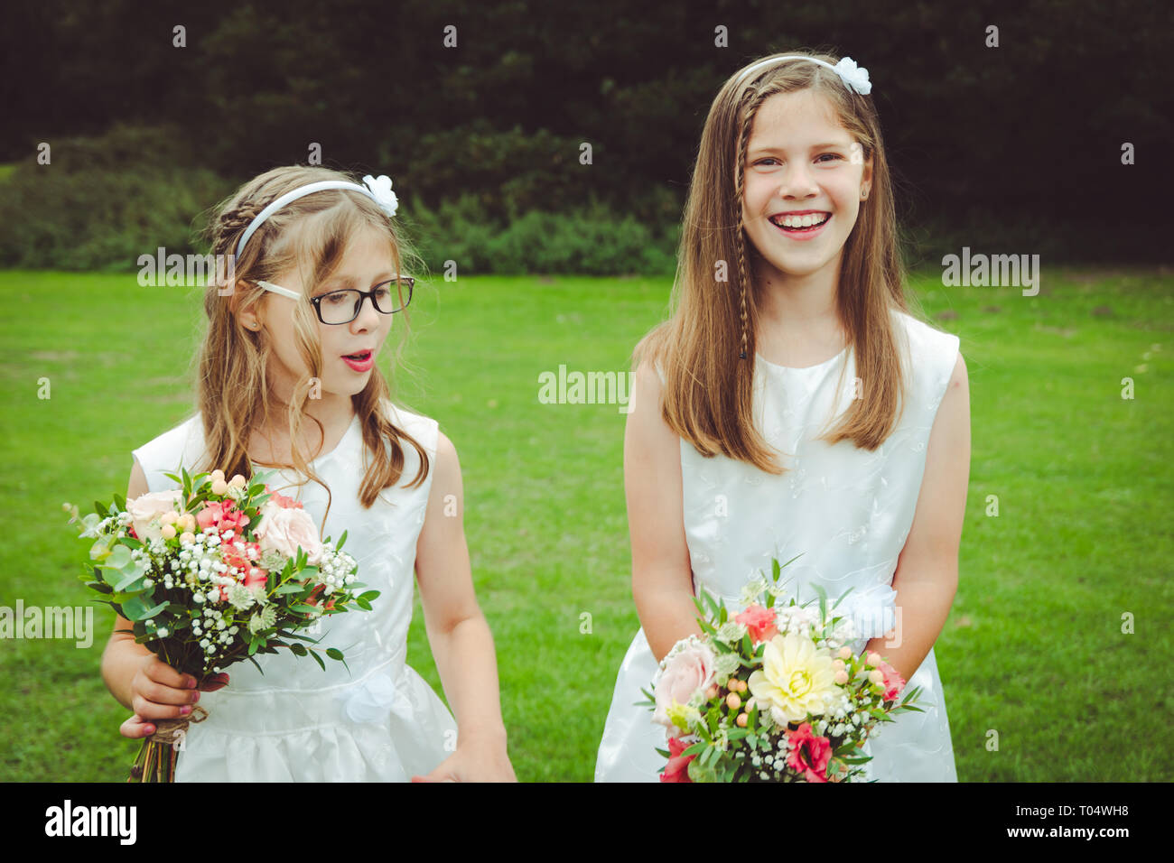 Schöne glücklich lächelnde Kind und Tween oder jugendlich Mädchen Brautjungfern in weißen Kleidern die Hand - saisonale Blumensträuße in einem Park gebunden Stockfoto