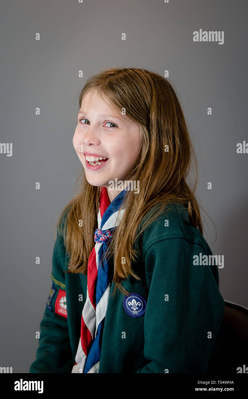 Ein portrait Foto von einem Lachen britischen Mädchen weibliche cub Scout in Uniform mit grünen Sweatshirt, roten, weißen und blauen Halstuch und Schieberegler oder woggle Stockfoto