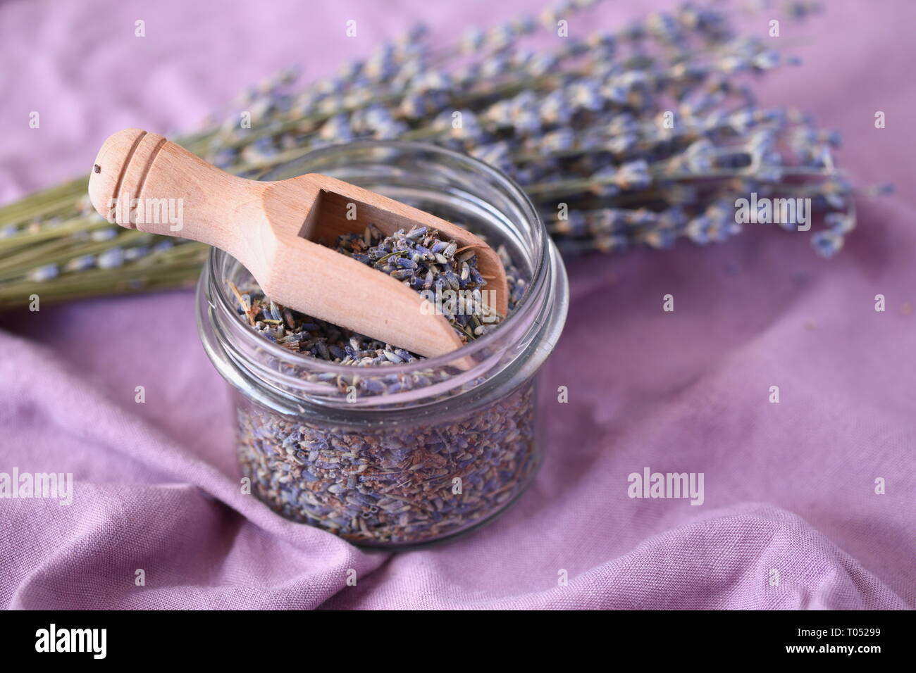 Getrocknete Lavendelblüten in einem Glas gegen Bündel von Lavendel Stockfoto