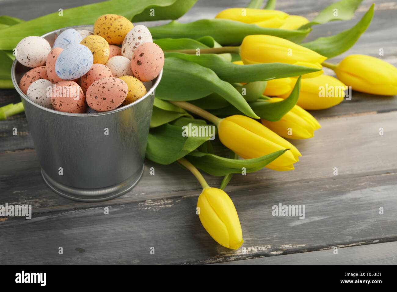 Bunte Ostern Süßigkeiten Eier mit gelben Tulpen auf hölzernen Tisch Stockfoto