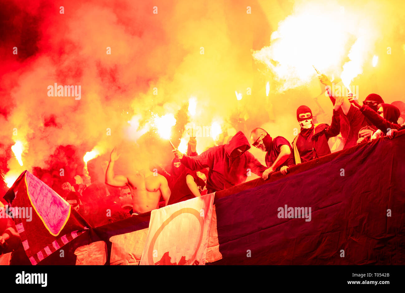 Fußball-Hooligans mit Maske halten Fackeln in Feuer, während Ihre Lieblingsmannschaft Unterstützung bei einem Spiel im Stadion Stockfoto