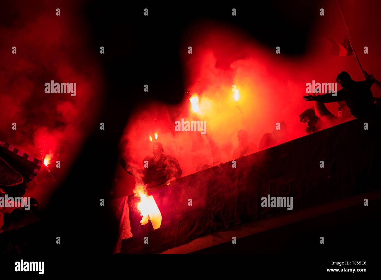 Fußball-Hooligans mit Maske halten Fackeln in Feuer, während Ihre Lieblingsmannschaft Unterstützung bei einem Spiel im Stadion Stockfoto