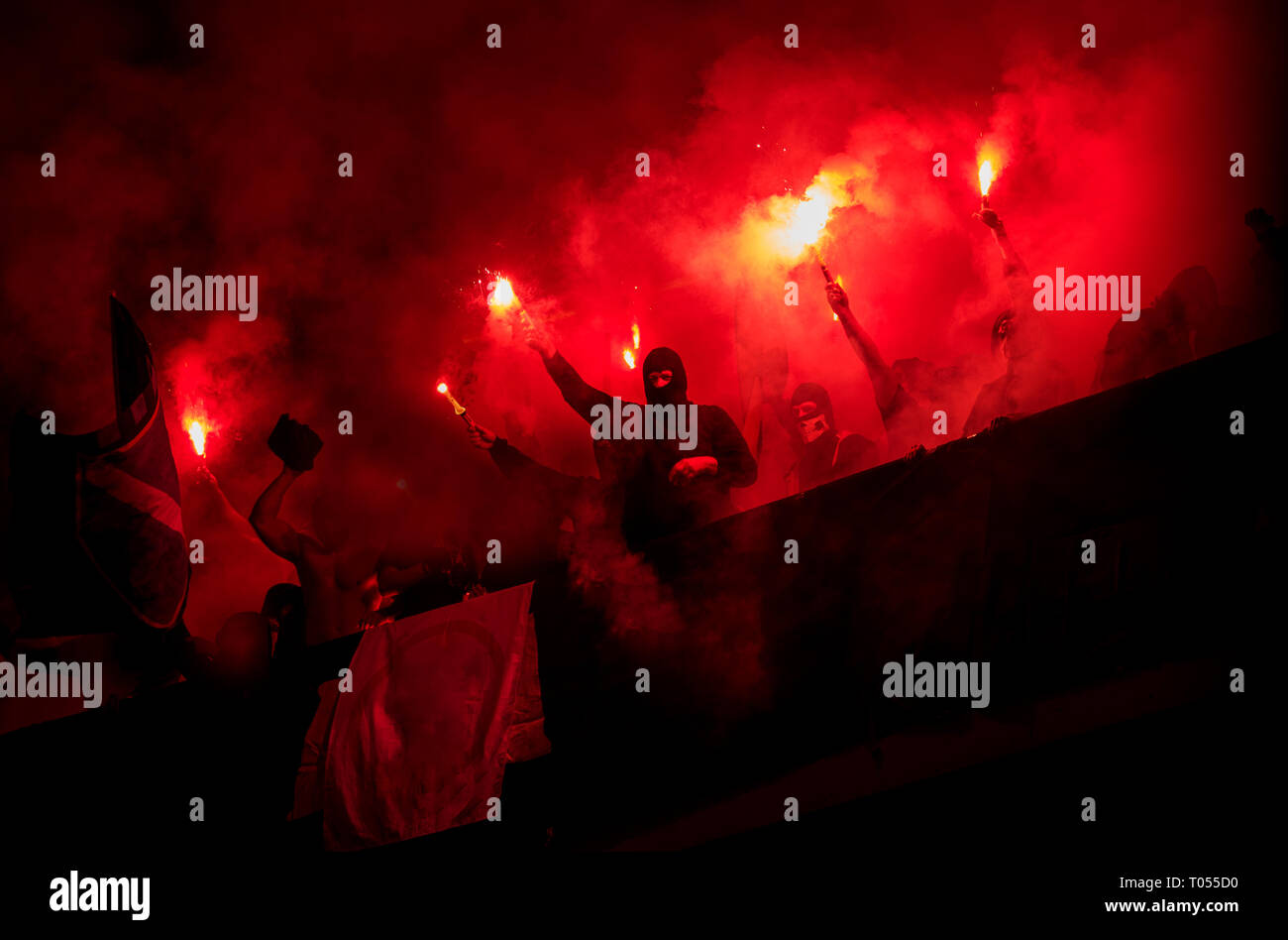 Fußball-Hooligans mit Maske halten Fackeln in Feuer, während Ihre Lieblingsmannschaft Unterstützung bei einem Spiel im Stadion Stockfoto