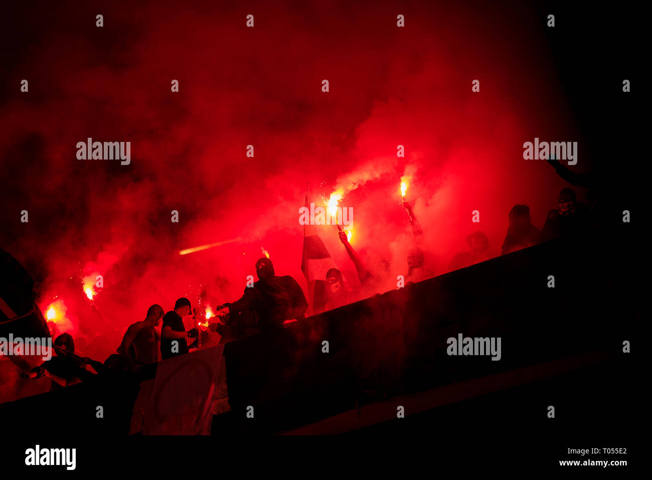 Fußball-Hooligans mit Maske halten Fackeln in Feuer, während Ihre Lieblingsmannschaft Unterstützung bei einem Spiel im Stadion Stockfoto