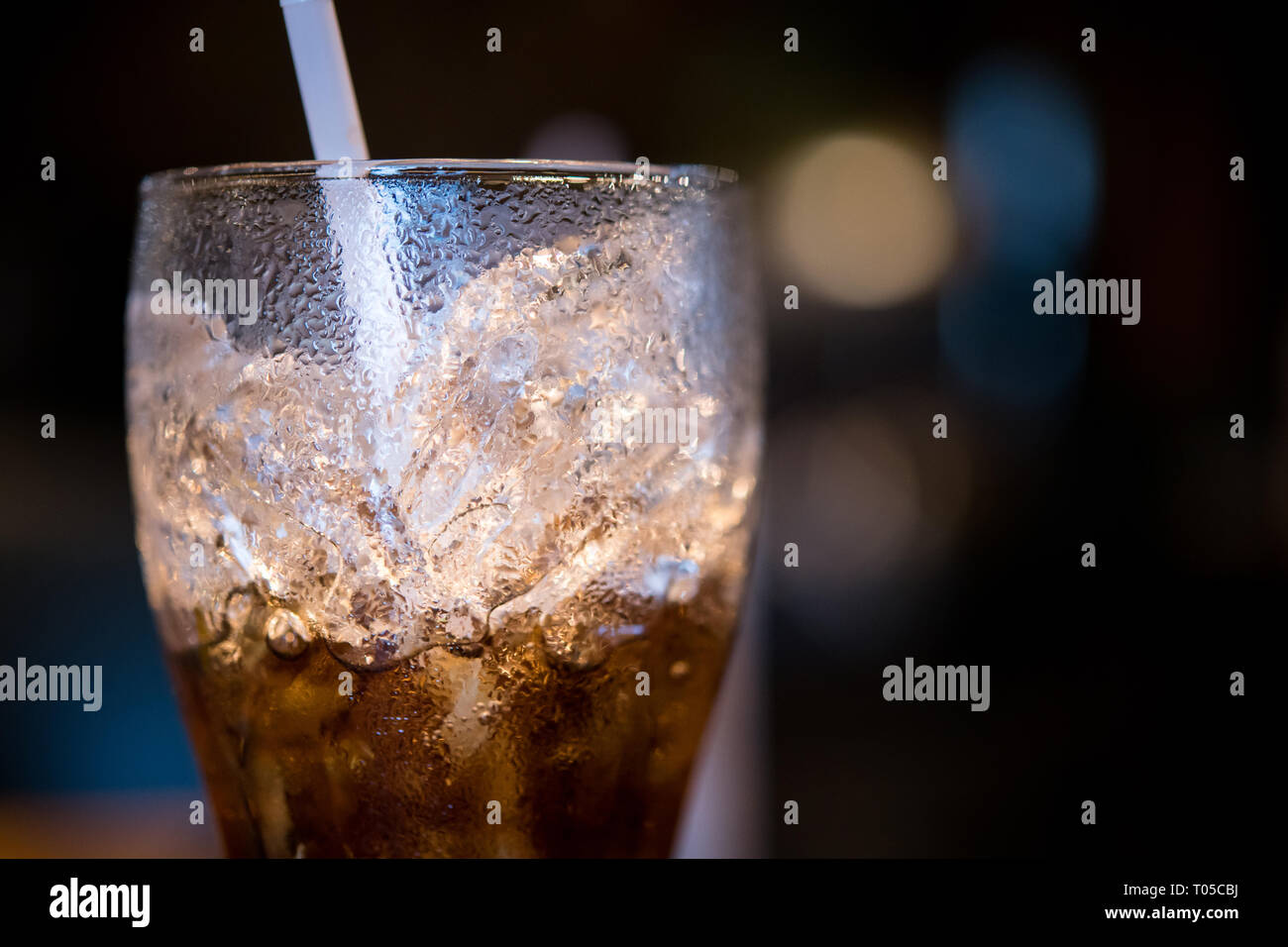 Glas halb Cola mit Eis und Stroh Stockfoto