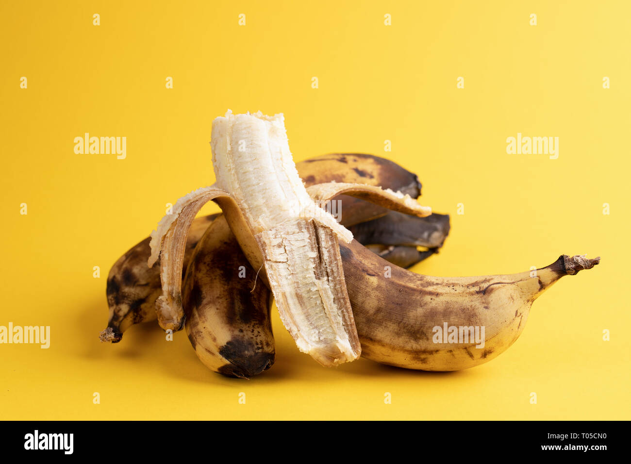 Close-up eine geschälte Banane und zwei ungeschält Überreifen geschwärzt hässlich Bananen auf gelben Hintergrund. Stockfoto