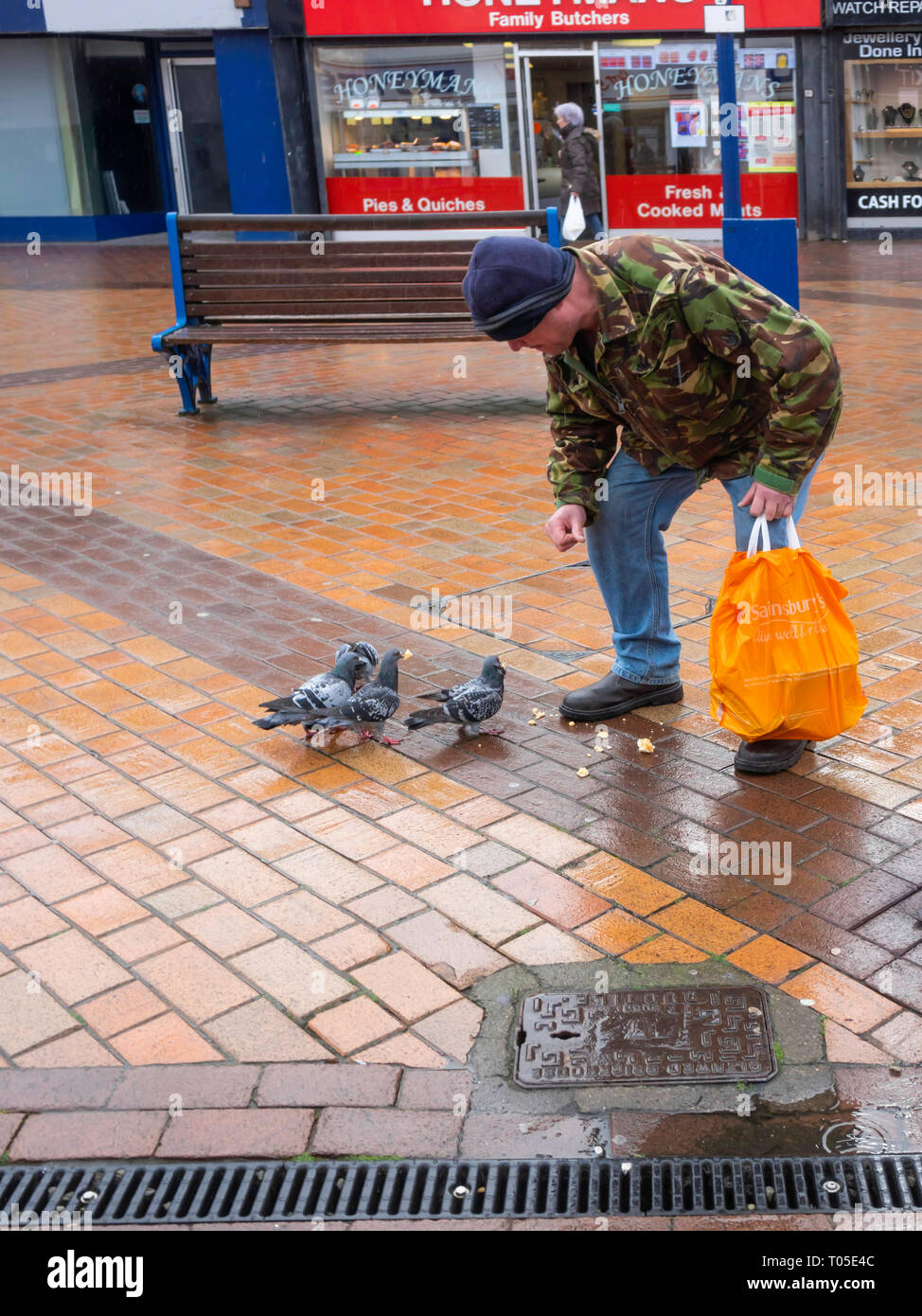 Ein Mann in einem Camouflage Jacke in Redcar Stadtzentrum füttern Tauben im Trotz der örtlichen Satzung verbietet, diese Praxis. Stockfoto