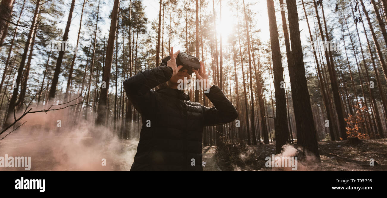 Frau im Wald mit Virtual reality Headset gerade Suchen mit orangen Rauch Rauchbomben Stockfoto