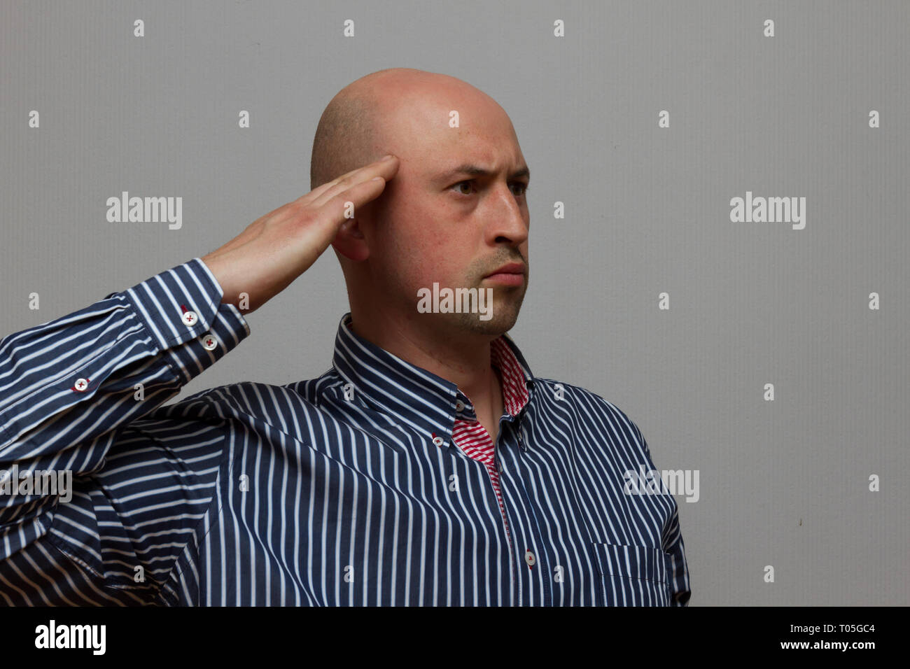 Junge glatzköpfige Mann salutierte auf grauem Hintergrund Stockfoto