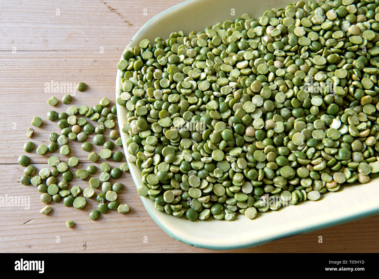 Geteilte Grüne Erbsen aus grüner Emailschale auf dem Küchentisch Stockfoto