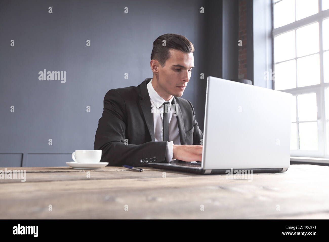 Junge Unternehmer im schwarzen Anzug mit Laptop im Büro Stockfoto