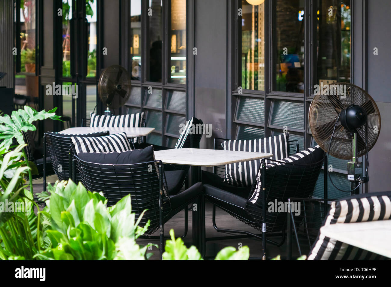 Eine einladende outdoor Marmor Tische und Stühle mit gemütlichen Kissen Schwarz und Weiß mit hellen grünen Pflanzen umgeben auf der Terrasse in Tag für Entspannung, Stockfoto