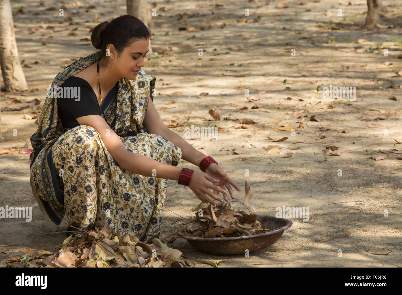 Ländliche Frau, gekleidet in Saree sammeln getrocknete Blätter vom Boden in einem Eisen Gold Pan. Stockfoto