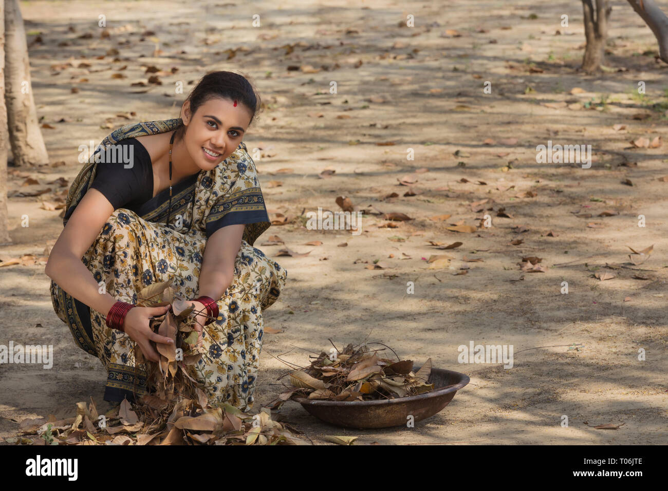 Ländliche Frau, gekleidet in Saree sammeln getrocknete Blätter vom Boden in einem Eisen Gold Pan. Stockfoto