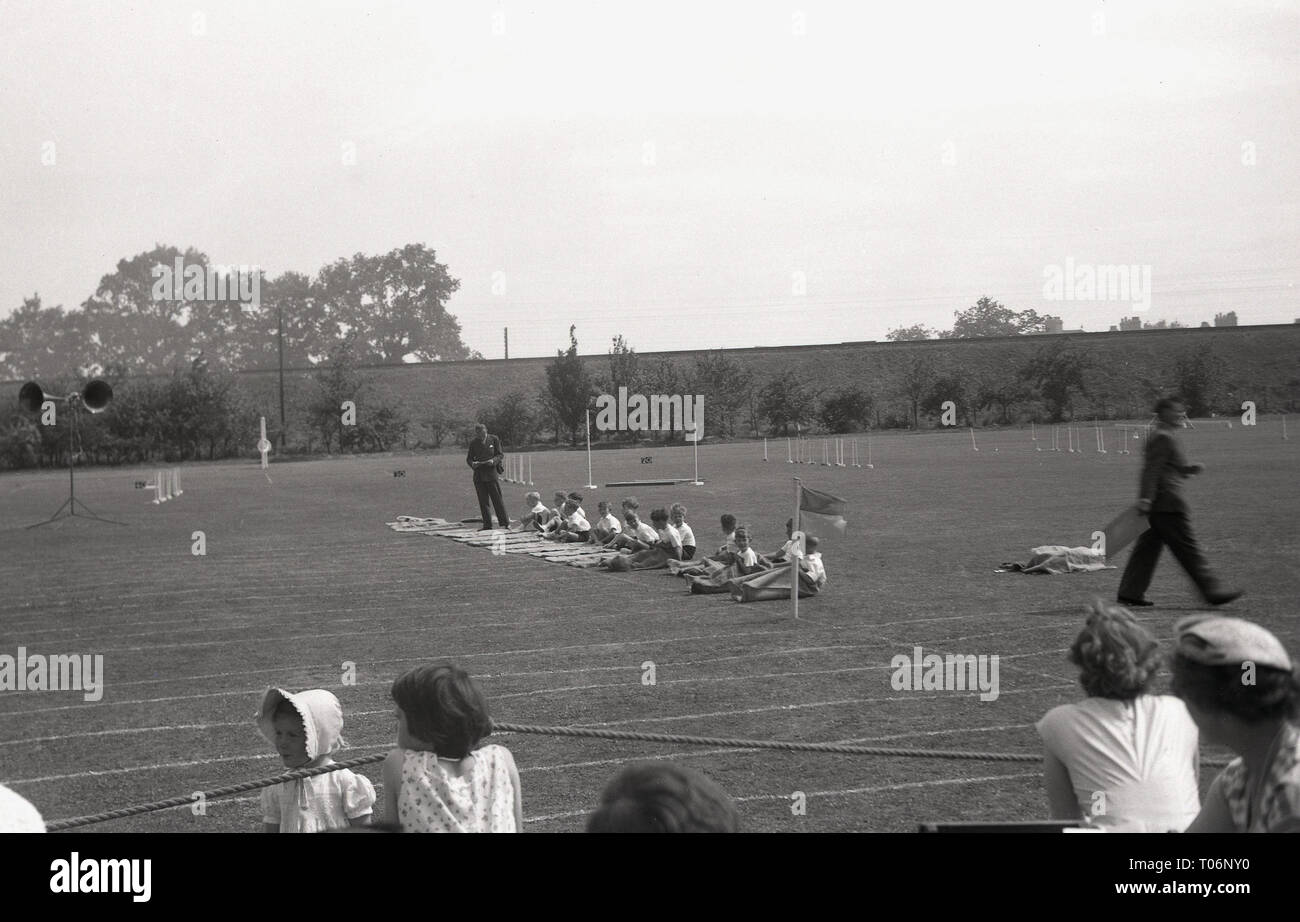 1950er Jahre, Sackhüpfen, Grundschule, Schüler draußen auf dem Sportplatz in ihre Säcke, England, UK. Stockfoto