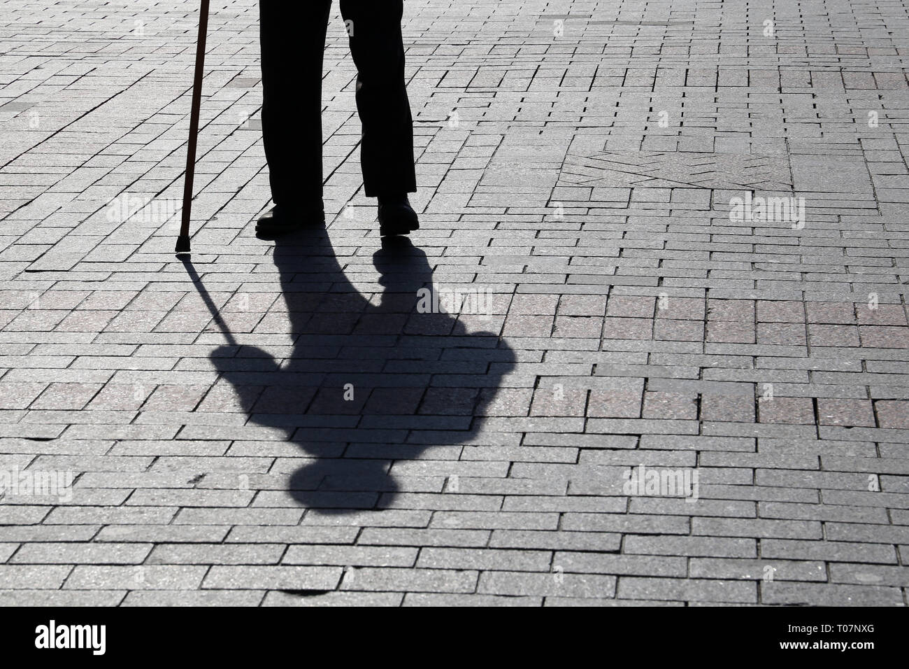 Silhouette der Mann mit einem Stock, lange Schatten auf Pflaster. Konzept der hinkt oder blind Person, Invalidität, Alter, Armut, Krankheiten der Wirbelsäule Stockfoto