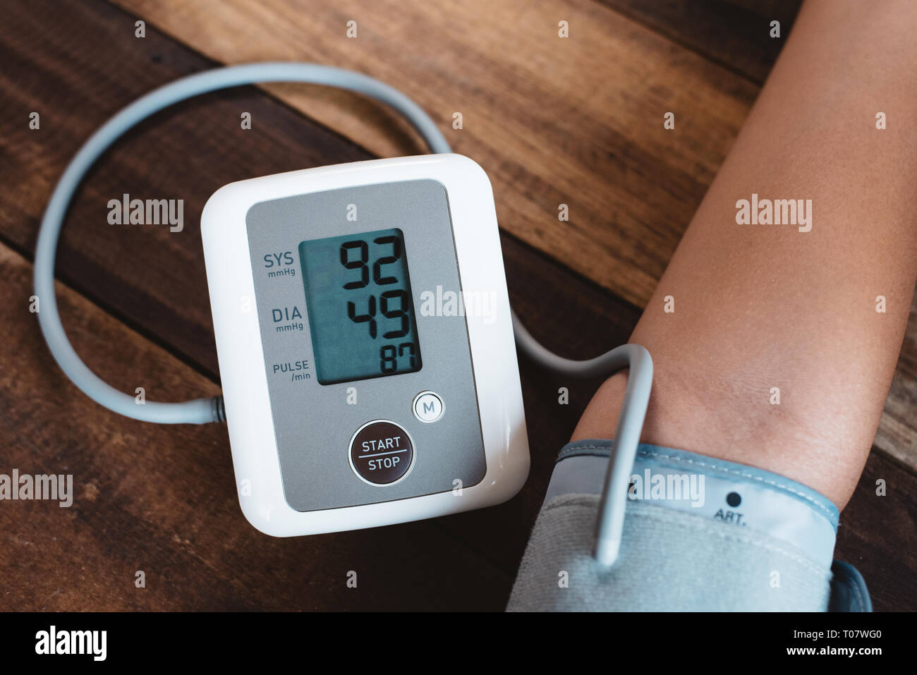 Der Mensch seinem Blutdruck mit elektronischen Blutdruckmessgerät oder Sphygmomanometer auf einem Holztisch. Konzept des Gesundheitswesen, medizinische instrume Stockfoto