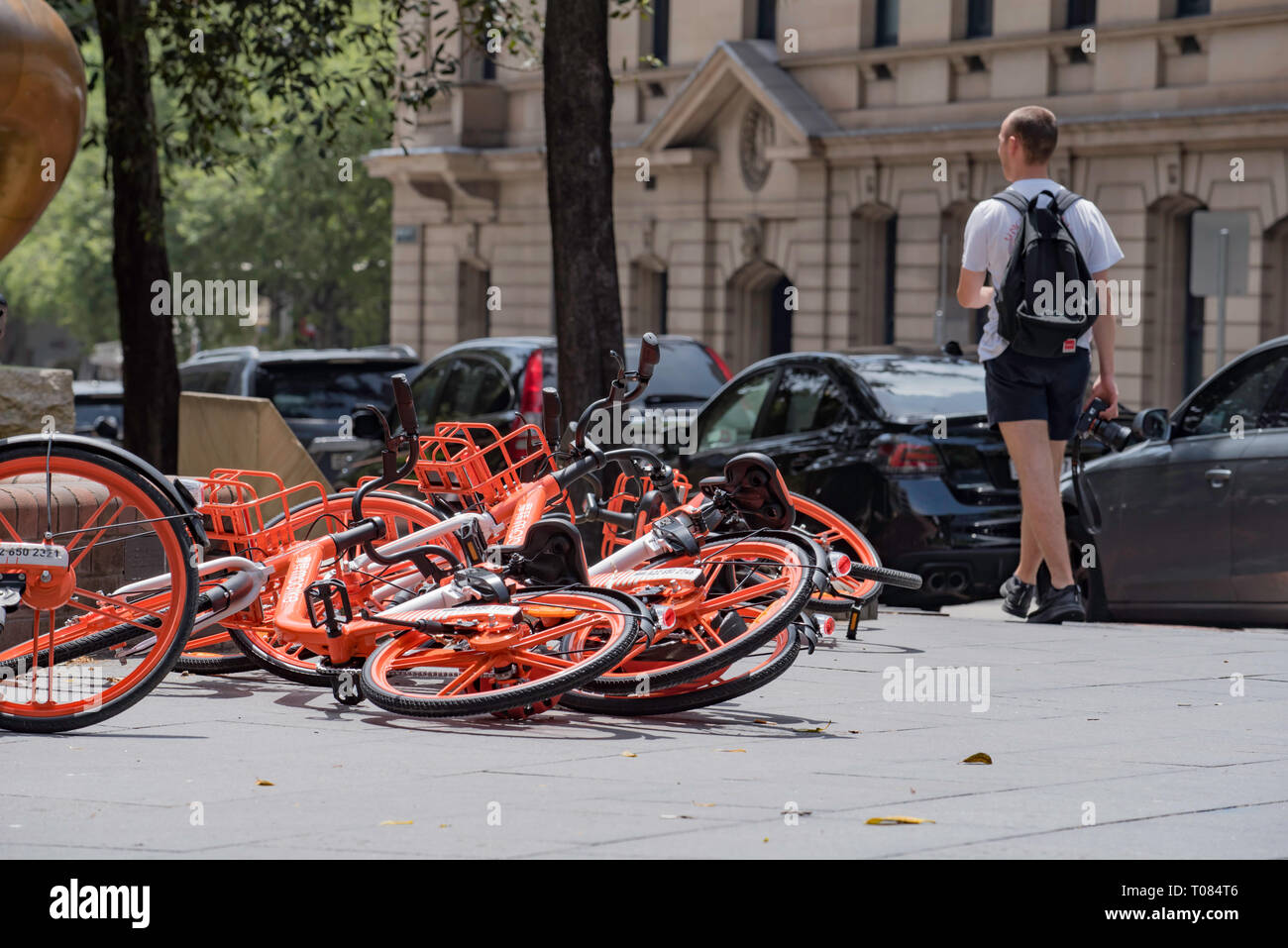 Eine junge weiße männliche Person mit einem Rucksack oder daypack geht hinunter Loftus Street in Sydney Australien Vergangenheit eine Sammlung von Fahrräder auf den Boden gefallen Stockfoto