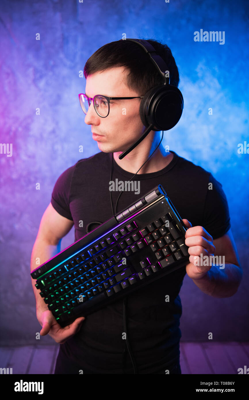 Technologie, Cyberspace, Programmierung und Personen Konzept - Hacker Mann in Headset und Brillen mit Tastatur über Neon Wand Stockfoto