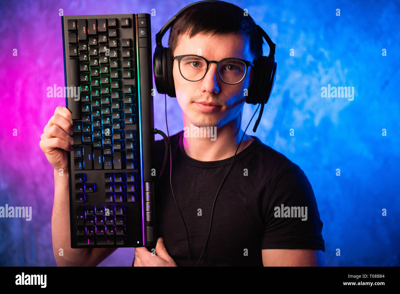 Technologie, Cyberspace, Programmierung und Personen Konzept - Hacker Mann in Headset und Brillen mit Tastatur über Neon Wand Stockfoto