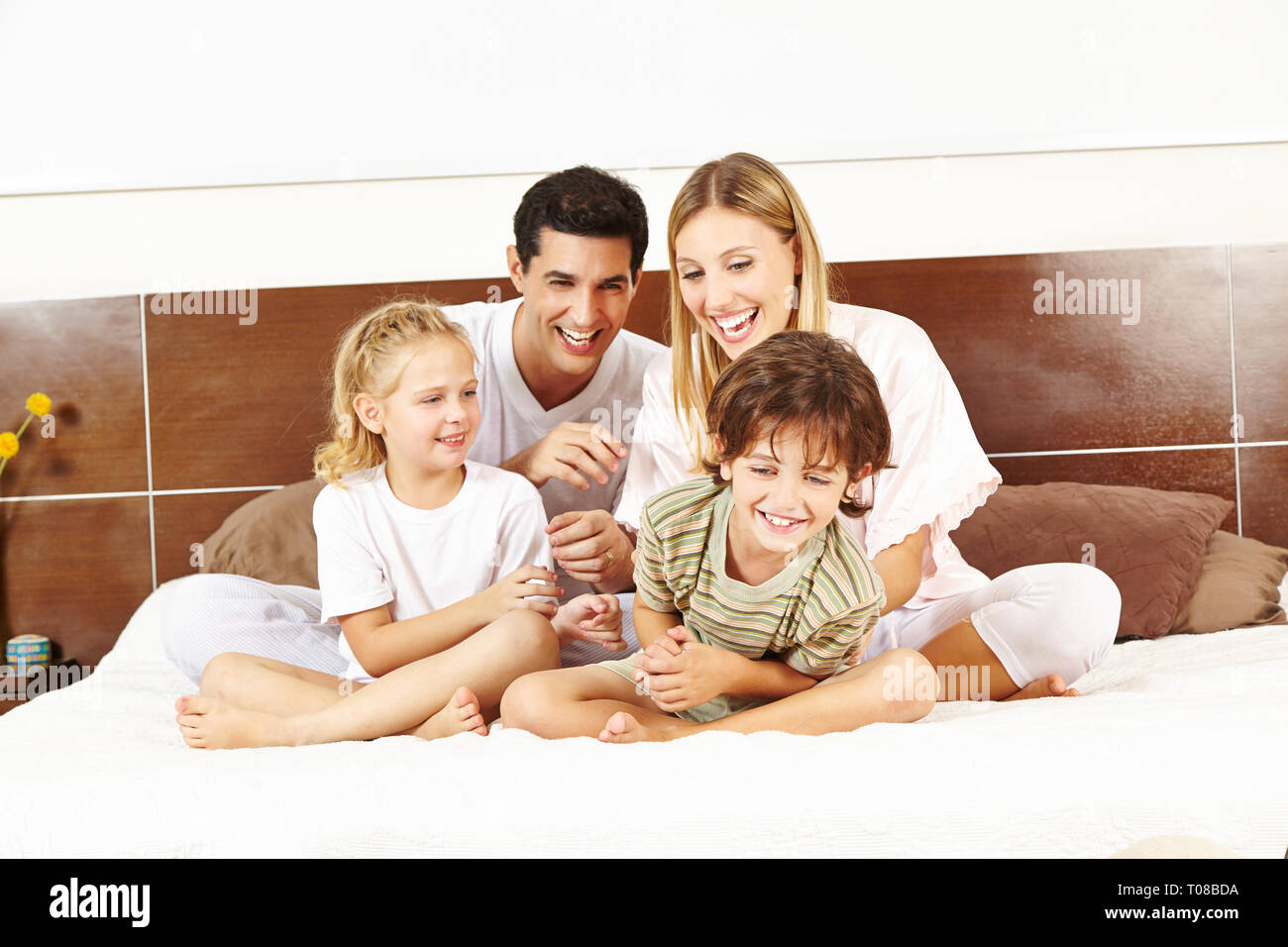 Lachend Familie sitzt im Bett mit zwei Kindern und Kitzeln einander Stockfoto