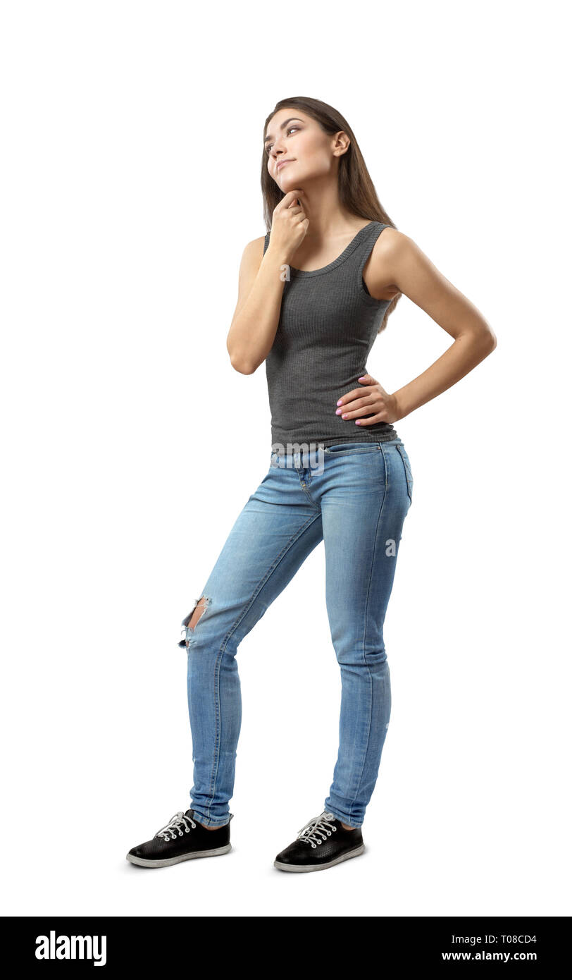 Junge Frau in ärmelloses Top und Jeans in der Hälfte stehend - drehen Sie mit der linken Hand auf die Hüfte und rechten Arm unter dem Kinn reiben auf weißem Hintergrund Stockfoto