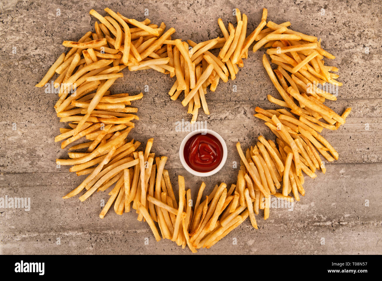 Nahaufnahme auf Herz Form von Pommes frites auf konkreten Hintergrund isoliert, Ketchup Schüssel in der Mitte. Direkt oberhalb. Stockfoto
