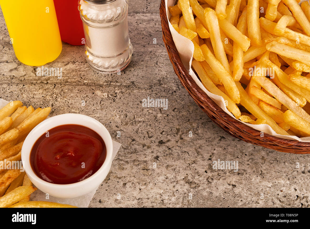 Warenkorb Pommes Frites mit Ketchup auf konkreten Hintergrund. Salz, Ketchup und Senf Flasche. Close Up. Stockfoto